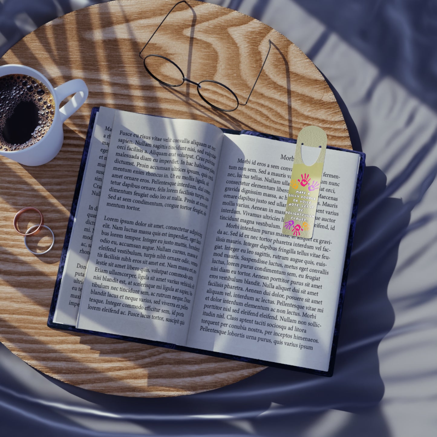 Open book with a colorful bookmark on a wooden table next to a cup of coffee and glasses.