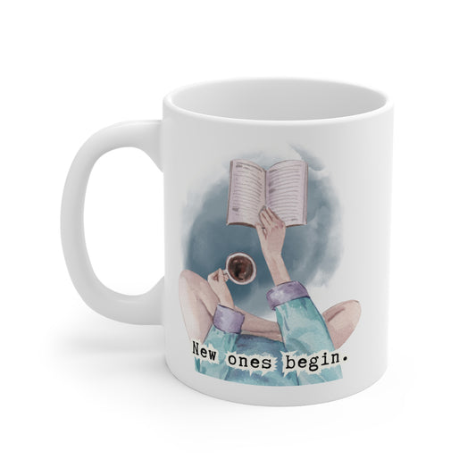 White mug with a design of hands reading a book and holding a cup, with the text 'New ones begin.'