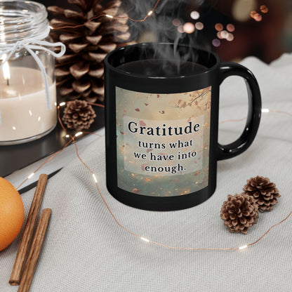 Black mug with 'Gratitude turns what we have into enough' quote, surrounded by decorative items on a table.