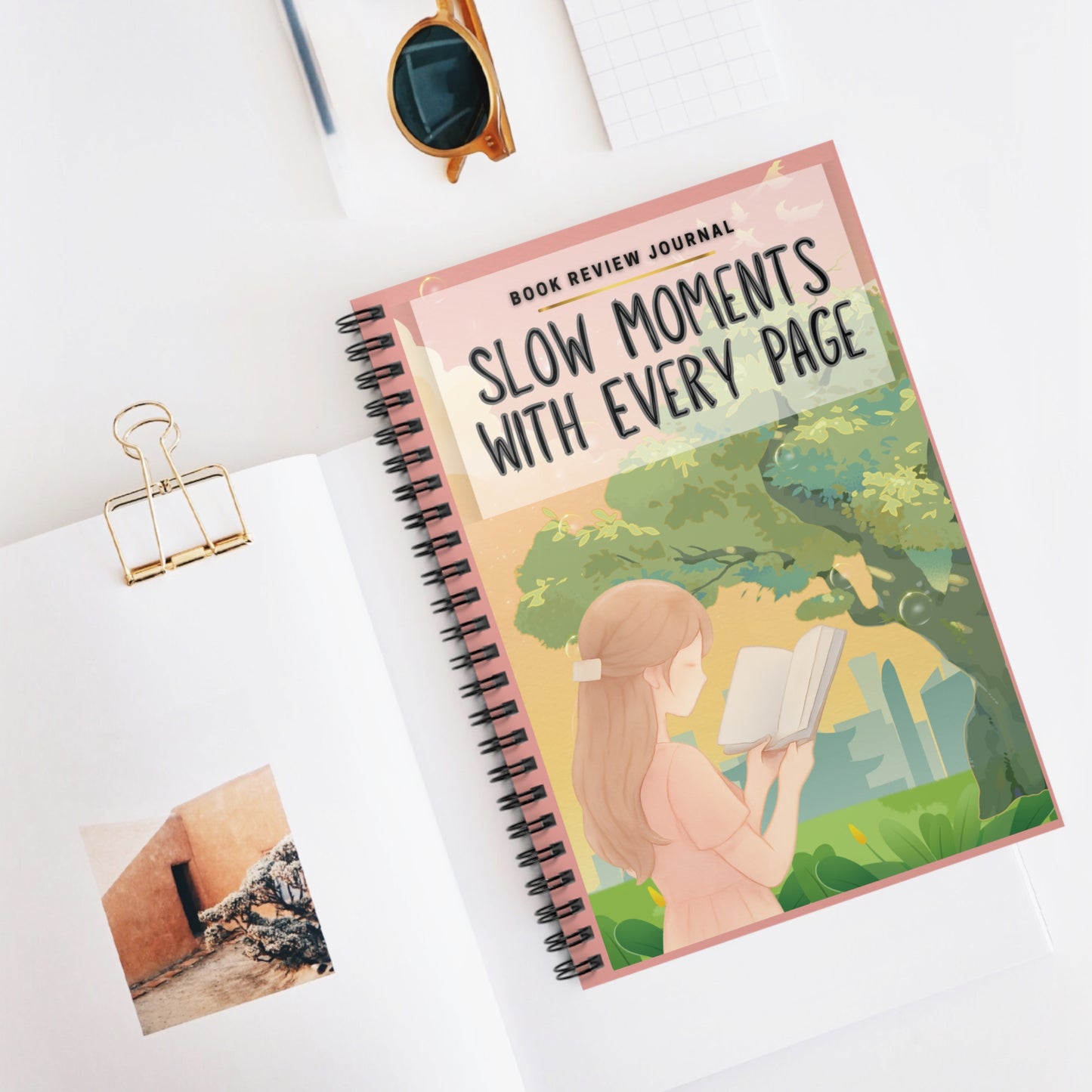 Notebook titled 'Slow Moments with Every Page' on a white surface with a clip and photo attached.