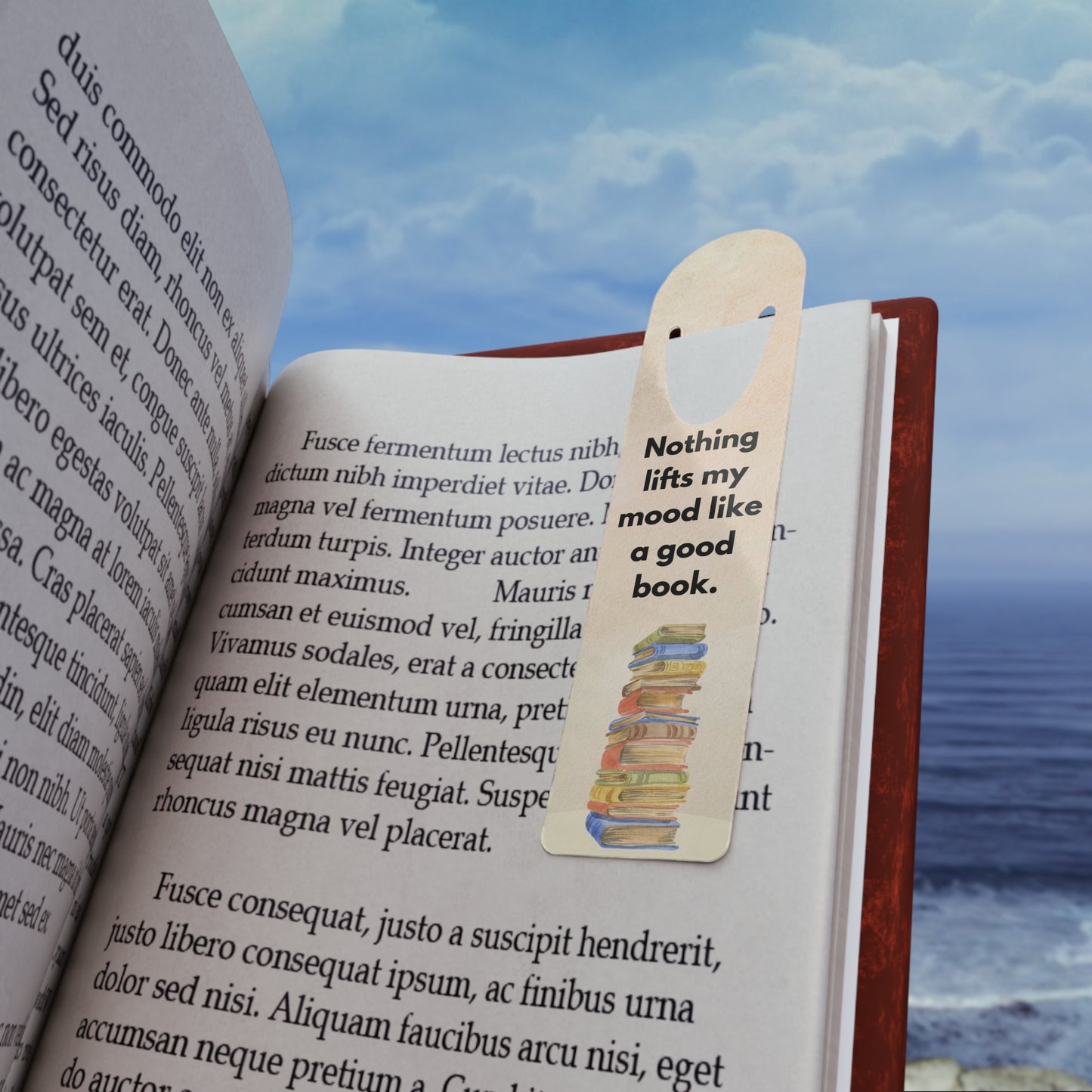 Open book with a bookmark featuring a quote, against a scenic background of water and sky.