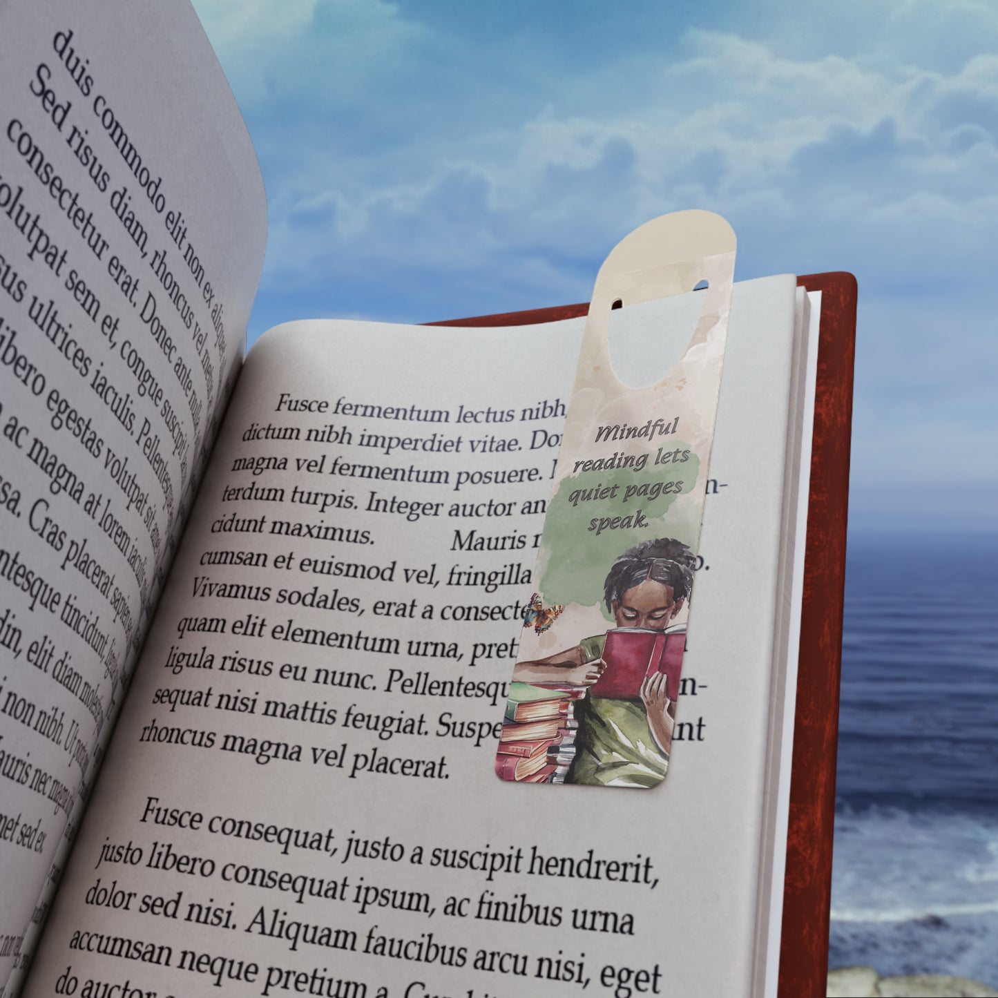 Open book with a bookmark featuring a person reading, against a scenic background of water and sky.