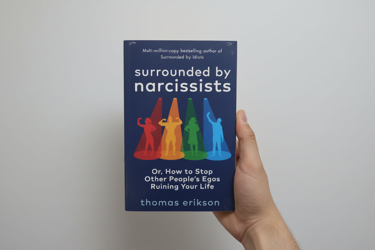 Book titled 'Surrounded by Narcissists' held by a hand against a blue background